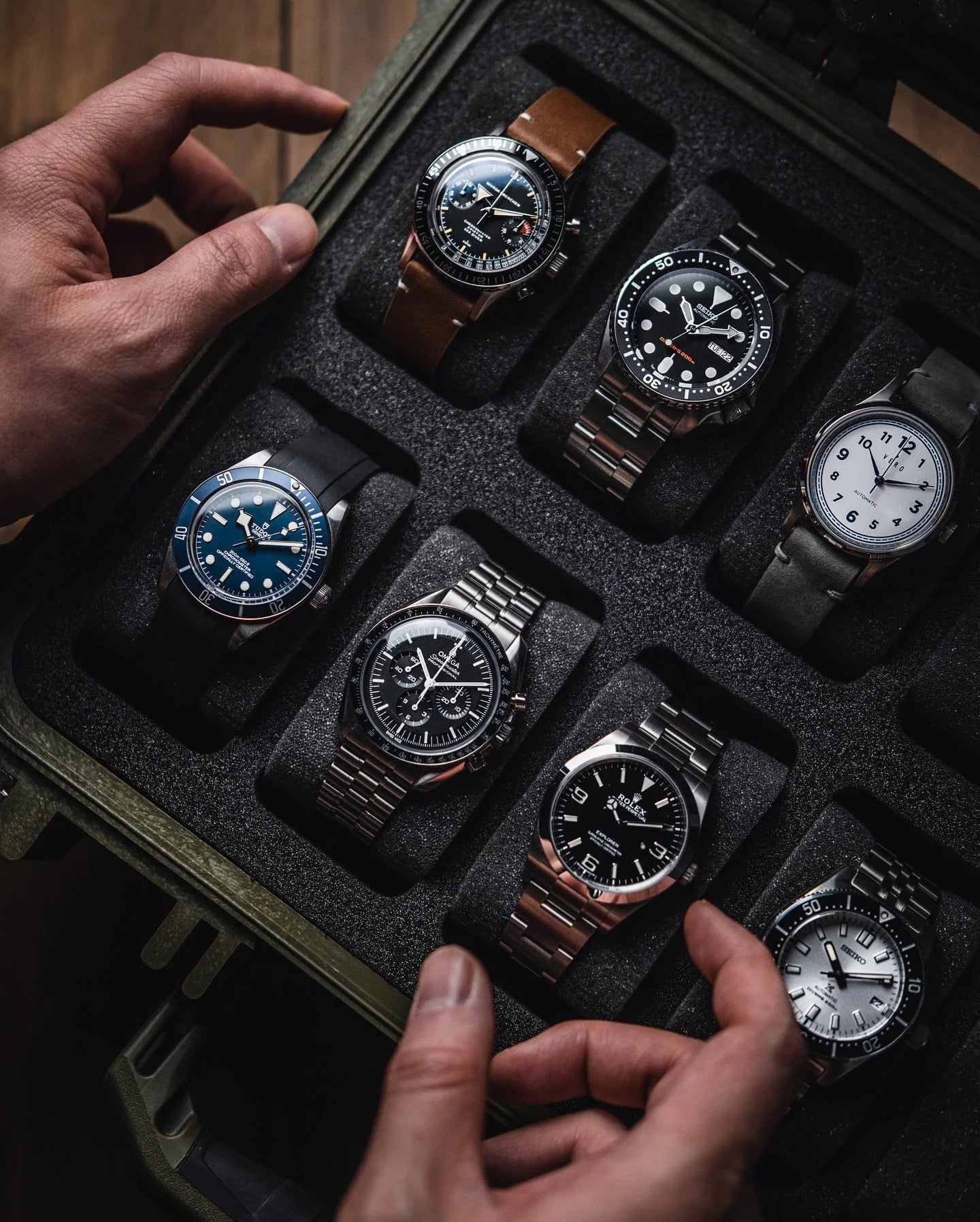 Collection of watches in a black display case with hands reaching towards them.